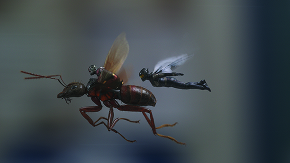 A small dark humanoid figure flies horizontally next to a large reddish-brown ant.