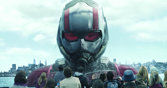 A massive figure in a silver and red helmet towers over a crowd of people near a city skyline.