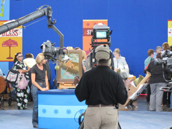A camera operator and crew film a scene in a studio with a blue backdrop and various props.