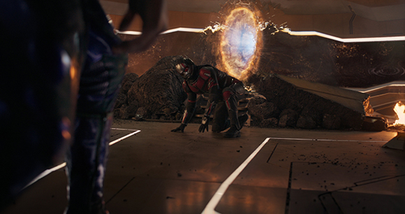 A person in a dark suit crouches on a floor near a glowing, circular portal in a dark room.