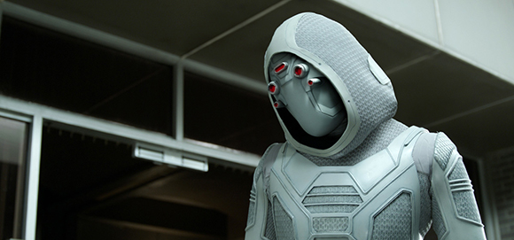 A person wearing a white, textured, futuristic armored suit and a hooded helmet with red eye sensors.