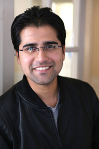 A smiling man with dark hair and glasses wearing a black leather jacket.