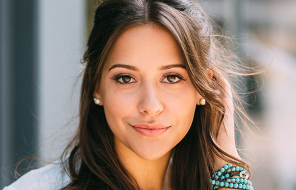 A woman with long brown hair and brown eyes looks directly at the camera.