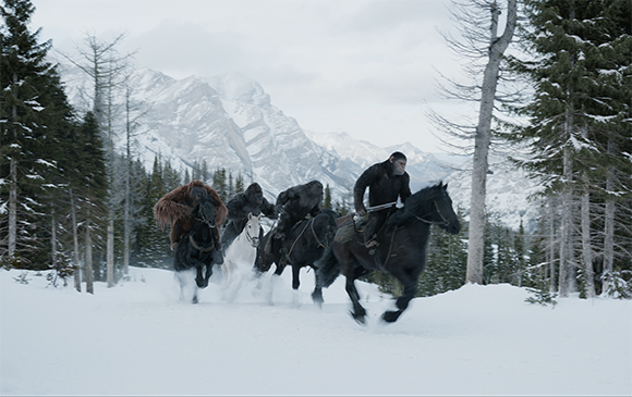 Four apes riding horses through a snowy forest with mountains in the background.