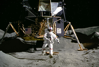 An astronaut in a white spacesuit walks across the cratered lunar surface near a lunar module.