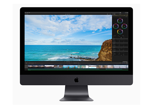 An Apple iMac displaying video editing software with a coastal landscape on the screen.