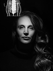 Black and white portrait of a woman with long wavy hair looking forward under a soft light.