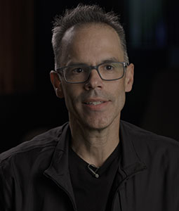 A man with short graying hair and glasses wearing a black jacket.