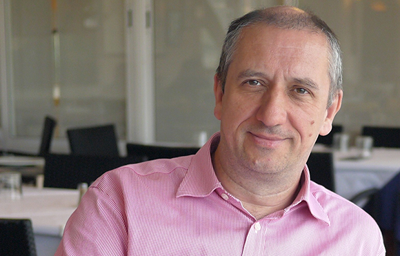 A man with short hair wearing a pink button-down shirt, smiling at the camera.