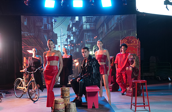 Six models in red and black fashion posing in a studio with a dark city backdrop.