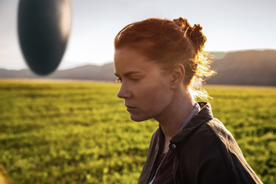 Profile of a red-haired woman looking down in a sunlit green field.