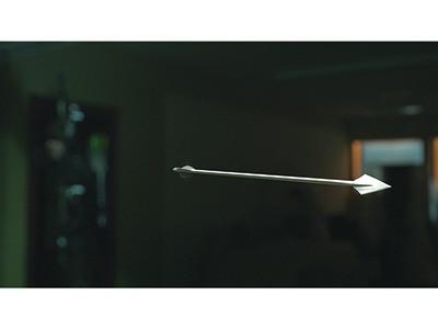A white arrow flying horizontally through a dark, blurred indoor setting.