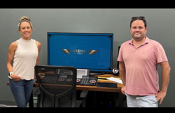 A man and a woman stand beside a desk with a computer monitor showing the Arsenal logo.