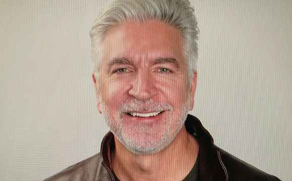 A smiling man with short gray hair and a salt-and-pepper beard looking toward the camera.