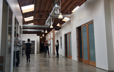 People walking and standing in a bright, modern office hallway with high ceilings and wooden accents.