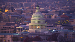 The illuminated white dome of the United States Capitol building against a twilight city skyline.