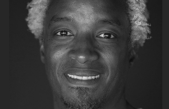 Black and white close-up portrait of a smiling man with curly hair and a goatee.