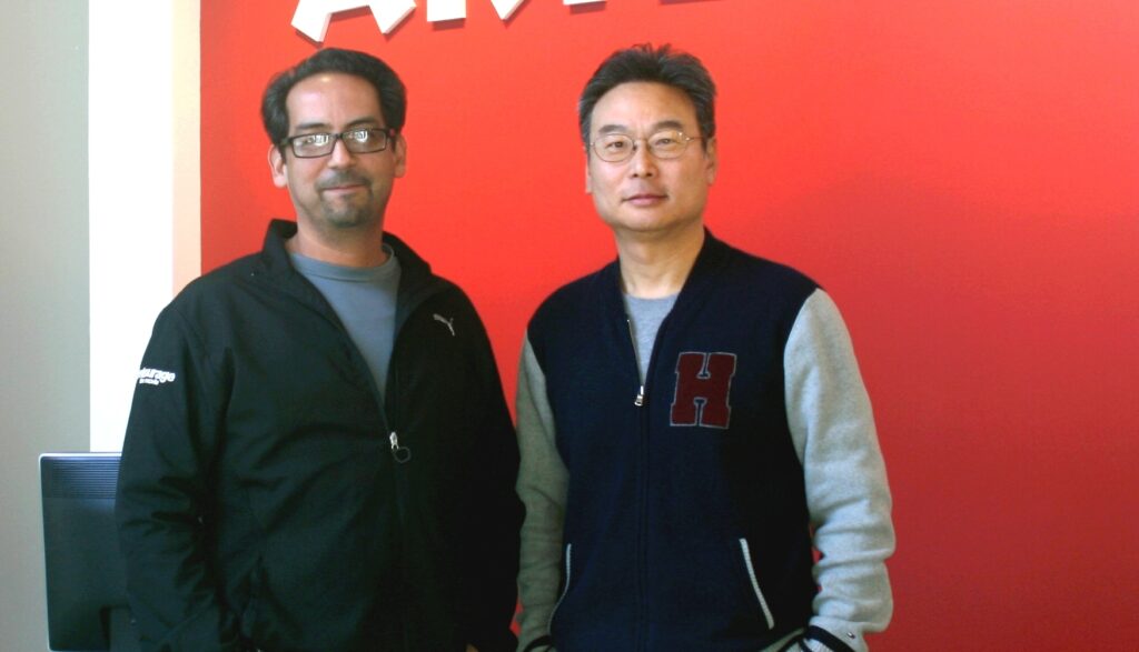 Two men posing together in front of a bright red wall.