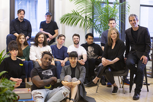 A group of twelve diverse people posing together in a bright, modern office space.