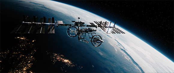 The International Space Station with solar arrays orbiting above the Earth's horizon against a starry sky.
