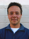 A man with short dark hair wearing a blue zip-up jacket over a white shirt.