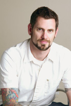 A man with short dark hair and a goatee wearing a white button-down shirt.