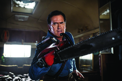 A man with a serious expression holds a large chainsaw in a dark, indoor setting.