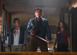 Three people with bloodstains on their clothes look upward in a dimly lit room.