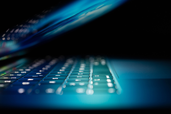 Close-up of a laptop keyboard with blue backlighting in a dark setting.