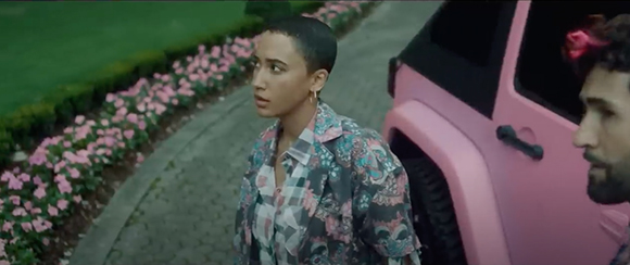 A woman with short hair in a patterned shirt looks toward a man standing by a pink SUV.