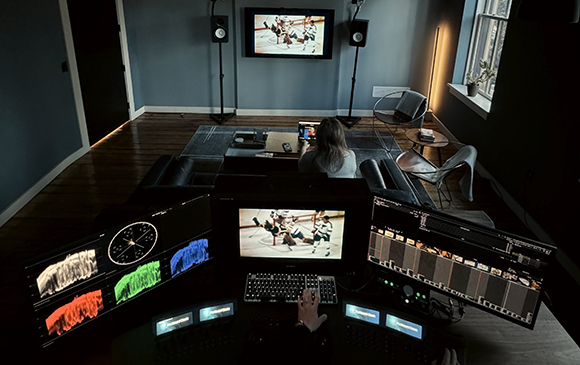 A person sits in a dark studio viewing video editing software and footage on several monitors.