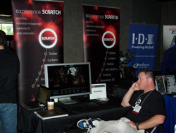 A man sits at a display booth featuring computer monitors and 'Experience Scratch' banners.