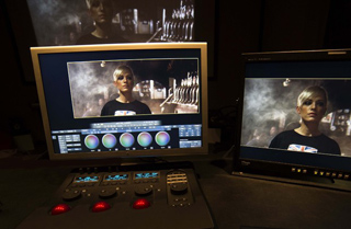Two computer monitors displaying a cinematic shot of a woman in a dark setting, above a control console.