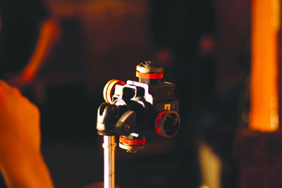 A black professional camera tripod head with red adjustment knobs on a metal stand against a dark background.