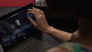 A person's hand reaches toward a laptop screen displaying a video editing interface.