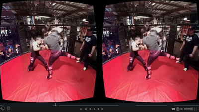 Two people practice martial arts in a red ring surrounded by a chain-link fence in a gym.