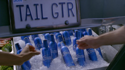 Hands reaching for blue beer bottles resting in a bed of ice under a sign that reads TAIL GTR.