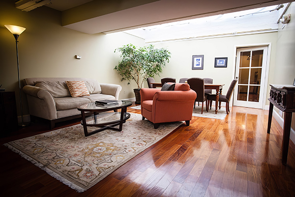 A living room with a beige sofa, orange armchair, and dining set under a large skylight.