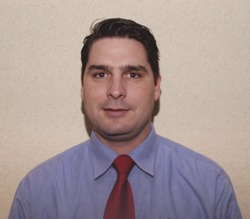A man with dark hair wearing a light blue button-down shirt and a solid red necktie.