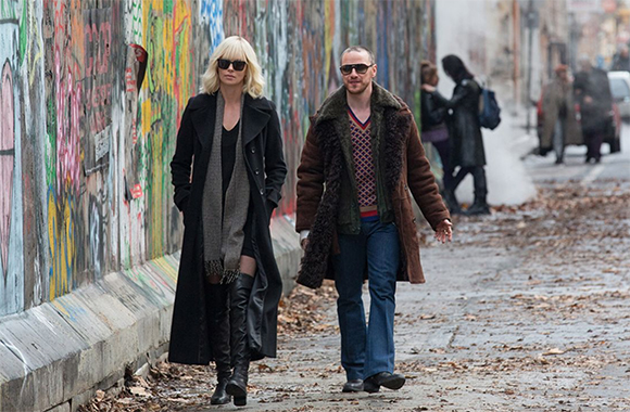A woman in a black coat and a man in a brown coat walk past a colorful graffiti wall.