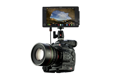 A black DSLR camera with a large lens and an external monitor displaying a landscape view on top.