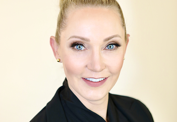 A smiling woman with blonde hair pulled back and blue eyes looking toward the camera.