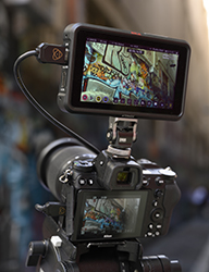 A professional camera mounted on a tripod with an attached external monitor showing a vibrant illustration.