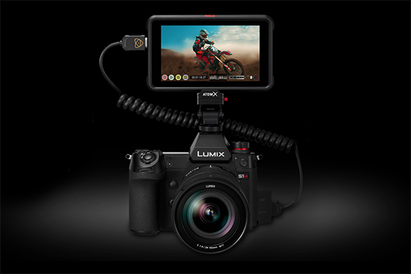 A black Lumix S1H camera with a large external monitor displaying a person riding a motorcycle.