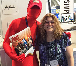 A woman in a patterned blue shirt smiles next to a person in a full red bodysuit holding a Post magazine.