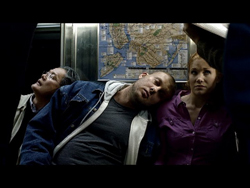 Three people sit closely together in a dark subway car near a transit map.