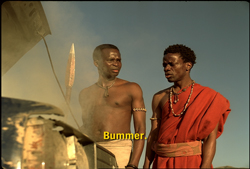 Two men in traditional attire look at an open car hood under a clear sky.