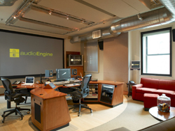 A recording studio featuring a large wooden desk, computer monitors, and a red leather sofa.