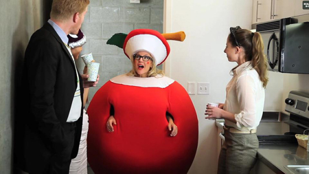 A person in a large tomato costume stands in a kitchen between three other people.