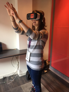 A woman wearing a VR headset and a striped sweater, with her hands raised and looking to her right.